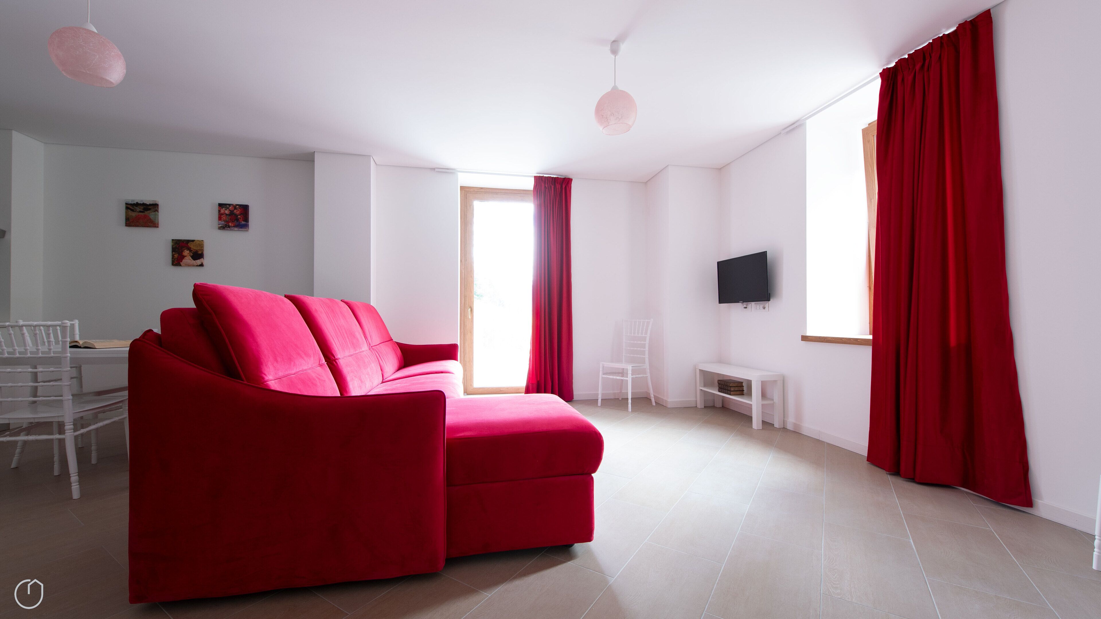 A modern living room with a red sofa, a white TV stand, and a large window with red curtains.