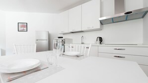 Une cuisine moderne avec des meubles blancs, une hotte en acier inoxydable et un coin repas avec une table blanche mise pour deux personnes.