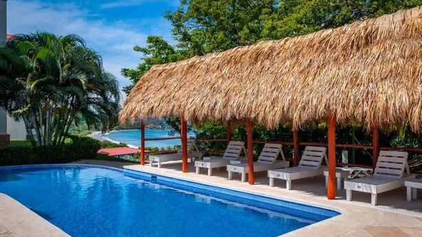 Piscina com espreguiçadeiras e uma cobertura de palha.