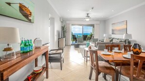 Quarto de hotel moderno com área de refeições, varanda com vista para o oceano e ventoinha no teto.
