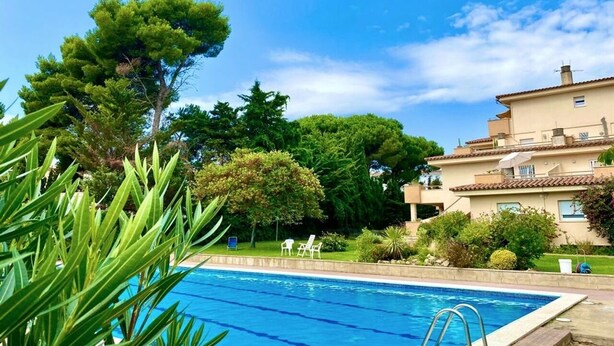 A swimming pool surrounded by lush greenery and a building with a tiled roof. - Apartment on the beach 300 meters from the sea, wifi, pool and tennis, ideal for families (L'Escala)