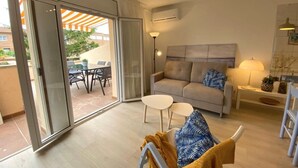 A modern living room with a sofa, a small table, and a sliding glass door leading to an outdoor patio area. - Apartment on the beach 300 meters from the sea, wifi, pool and tennis, ideal for families (L'Escala)