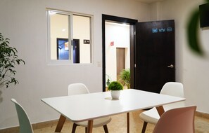 A conference room with a white table, four chairs, a potted plant, and a door with symbols indicating amenities. - Nora Hotel & Co living (Guadalajara)