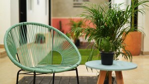 Una silla de mimbre verde y una mesita con una planta en maceta en un pasillo.