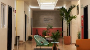 Un vestíbulo moderno con techo alto, barandillas de vidrio, una zona de estar central con una silla verde y plantas en macetas.