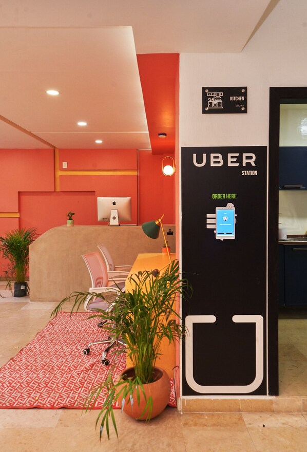 A modern interior with a reception desk, a sign for the kitchen, and an Uber station. - Nora Hotel & Co living (Guadalajara)