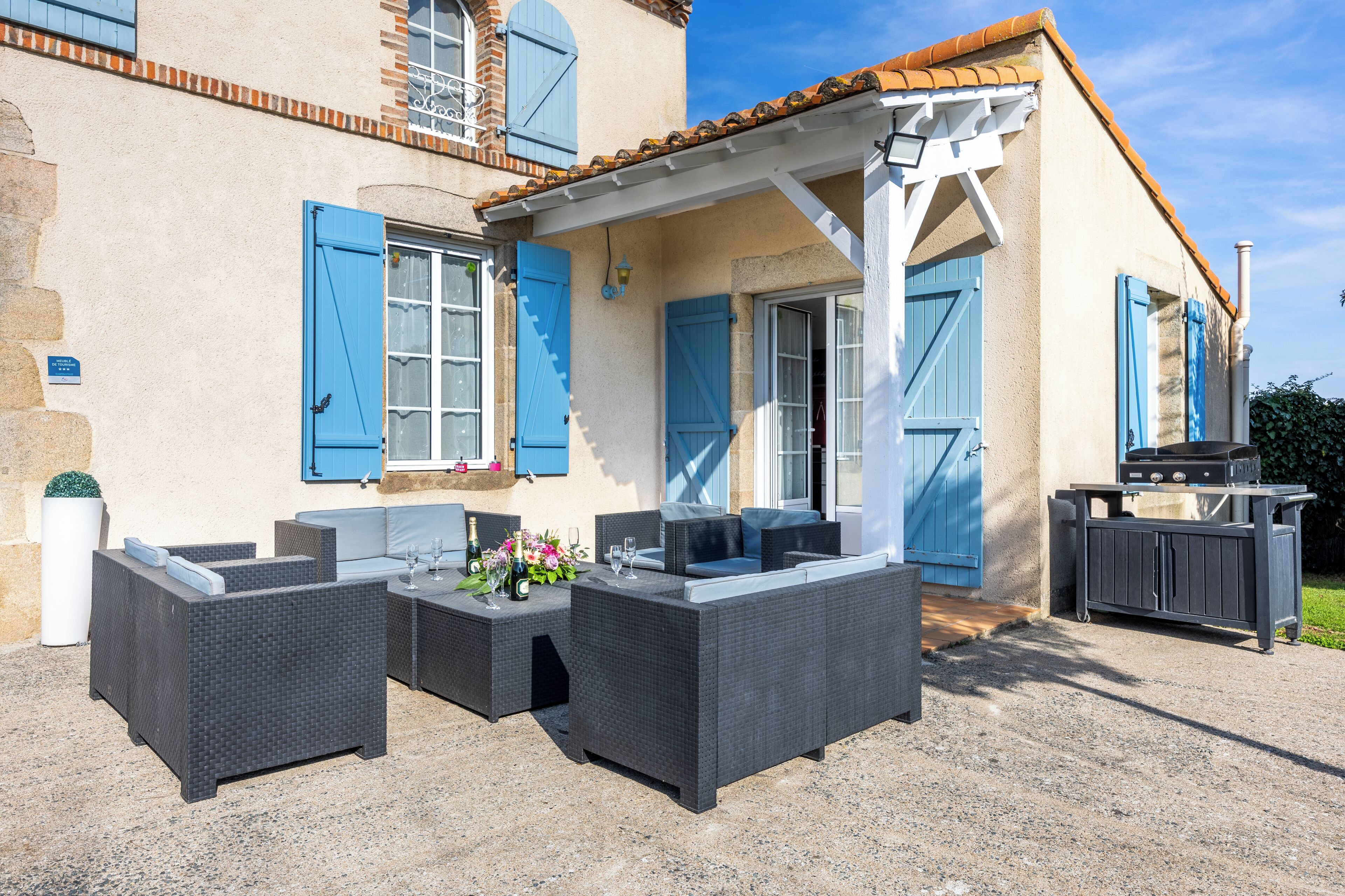 An outdoor seating area with wicker furniture, a barbecue grill, and a building with blue shutters.