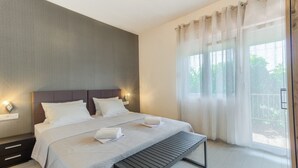 A modern bedroom with a large bed, bedside tables, and a view of greenery outside.
