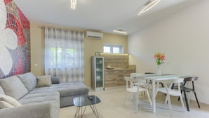 A modern living room with a grey sofa, a glass coffee table, and a dining area with white chairs and a glass table.