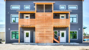 Un edificio moderno de dos pisos con una terraza de madera y una escalera que lleva al piso superior.