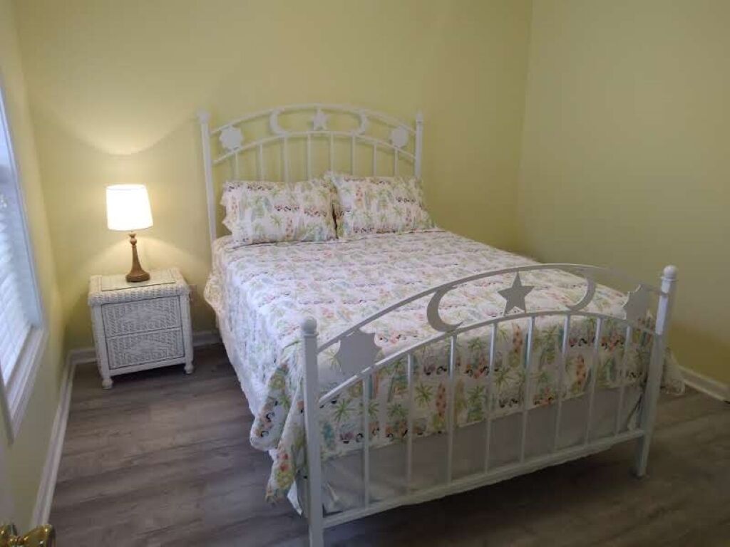 A white metal bed with floral bedding in a room with light yellow walls and a small bedside table with a lamp.