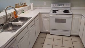 A kitchen with white cabinets, a stainless steel sink, a microwave, and a stove. - Nice, totally re modeled, 3 bedroom condo in the heart of Cherry Grove Beach (North Myrtle Beach)