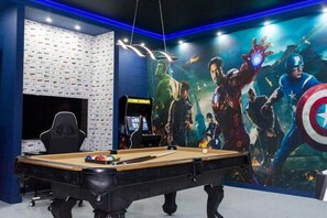 Ett rum med ett biljardbord, en gamingstol och en stor väggmålning med Avengers-tema.