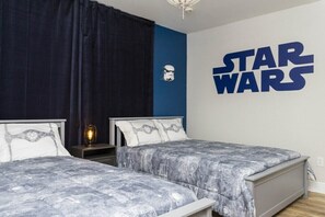 Ett sovrum med två sängar, en Star Wars-väggdekor och ett nattduksbord med en lampa.