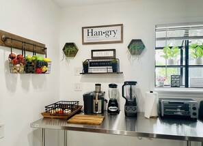 A kitchen with a hanging fruit basket, a blender, a toaster, and a window with plants.