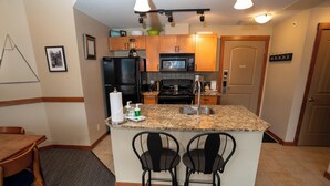 A compact kitchen with a central island, bar stools, a refrigerator, microwave, and a stove. - Enjoy Some of the Best Mountain Views In Canmore, Falcon Crest Lodge (Canmore)
