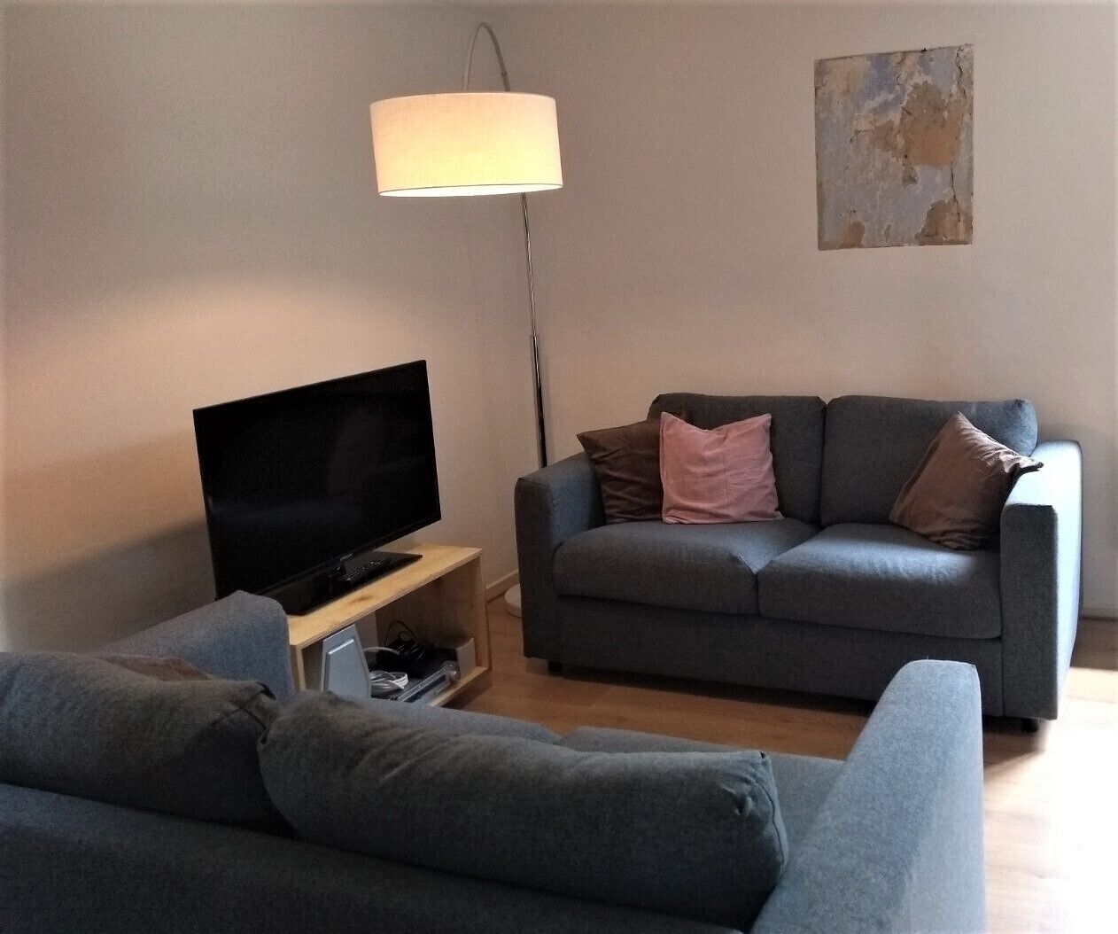 Un salon avec un téléviseur à écran plat posé sur un meuble en bois, un canapé gris agrémenté de coussins et un lampadaire.