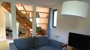 Un saló amb un sofà, una televisió sobre un suport de fusta, una escala i una finestra amb cortines.