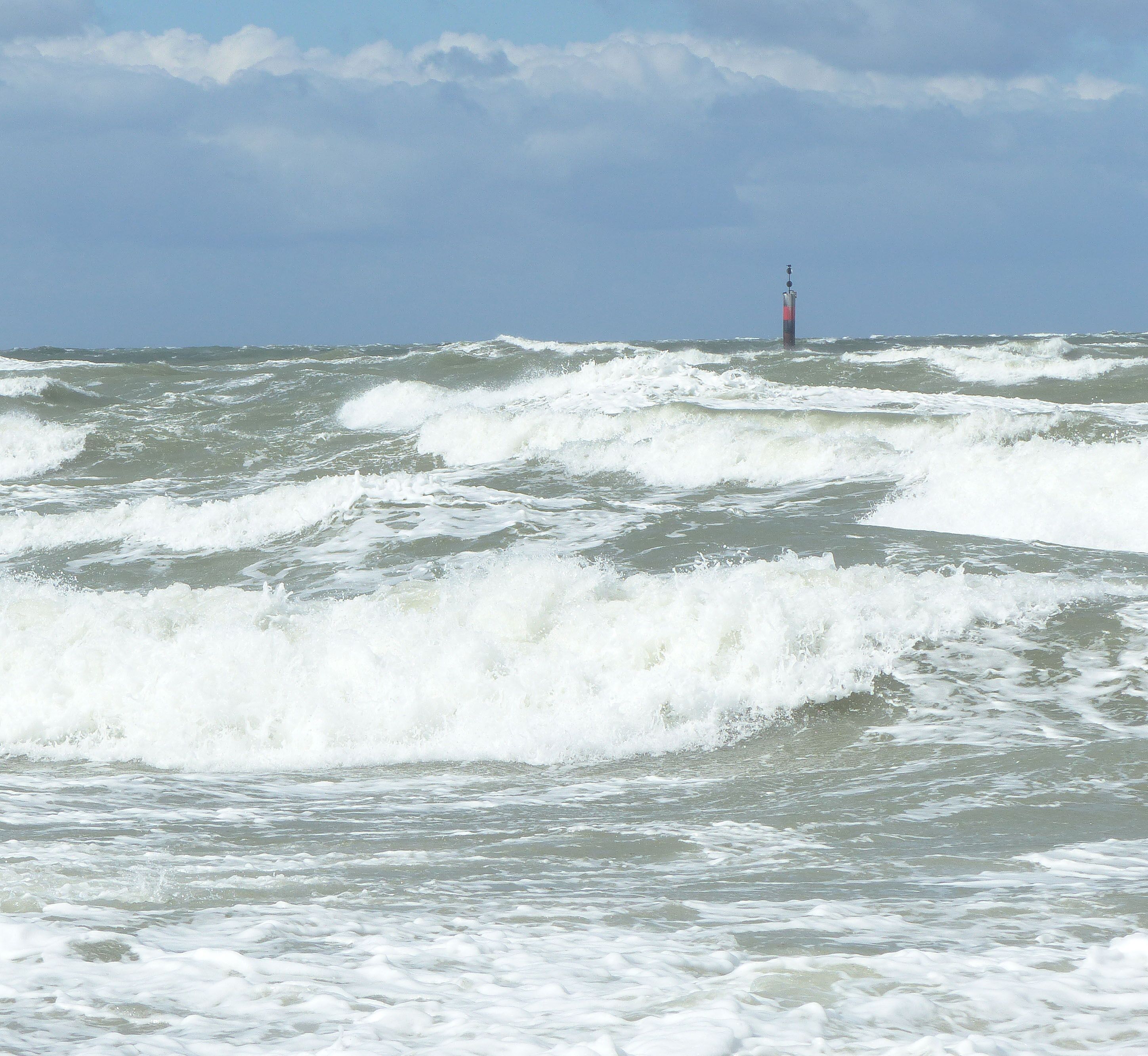 Un phare se dessine à l’horizon, tandis que des vagues agitées déferlent au premier plan.