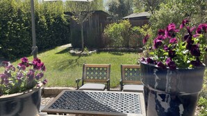 Una zona de pati amb taula i cadires, un parasol gran i plantes en testos.