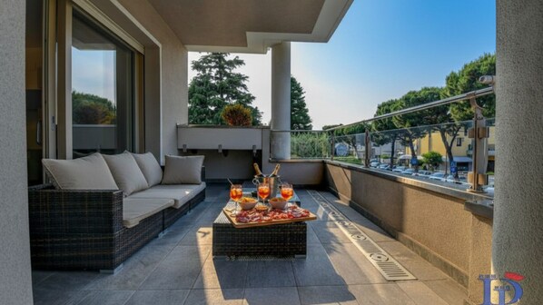 A balcony with a wicker sofa, a table with drinks and snacks, and a city view.