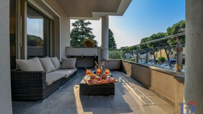 Un balcón con un sofá de mimbre, una mesa con bebidas y aperitivos, y vistas a la ciudad.