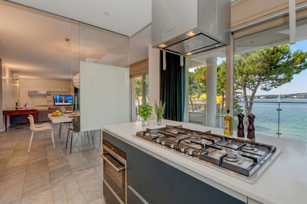 A modern kitchen with a large island, a dining area, and a view of the sea.