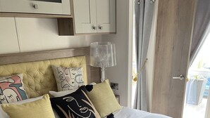 A bedroom with a bed, pillows, a lamp, a wardrobe, and a door.