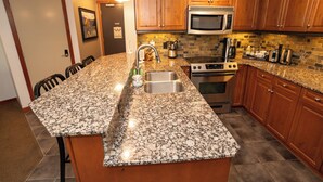 A kitchen with granite countertops, wooden cabinets, a stainless steel sink, a microwave, a stove, and a toaster. - Enjoy a Cozy Condo and Lots of Fun with Family Friendly Pool and Hot Tubs  (Canmore)