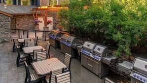 An outdoor patio with multiple barbecue grills and wooden tables and chairs. - Enjoy a Cozy Condo and Lots of Fun with Family Friendly Pool and Hot Tubs  (Canmore)