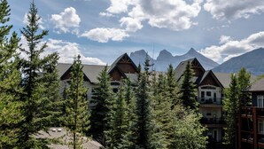 A mountain lodge with multiple buildings, surrounded by evergreen trees and a backdrop of snow-capped peaks. - Enjoy a Cozy Condo and Lots of Fun with Family Friendly Pool and Hot Tubs  (Canmore)