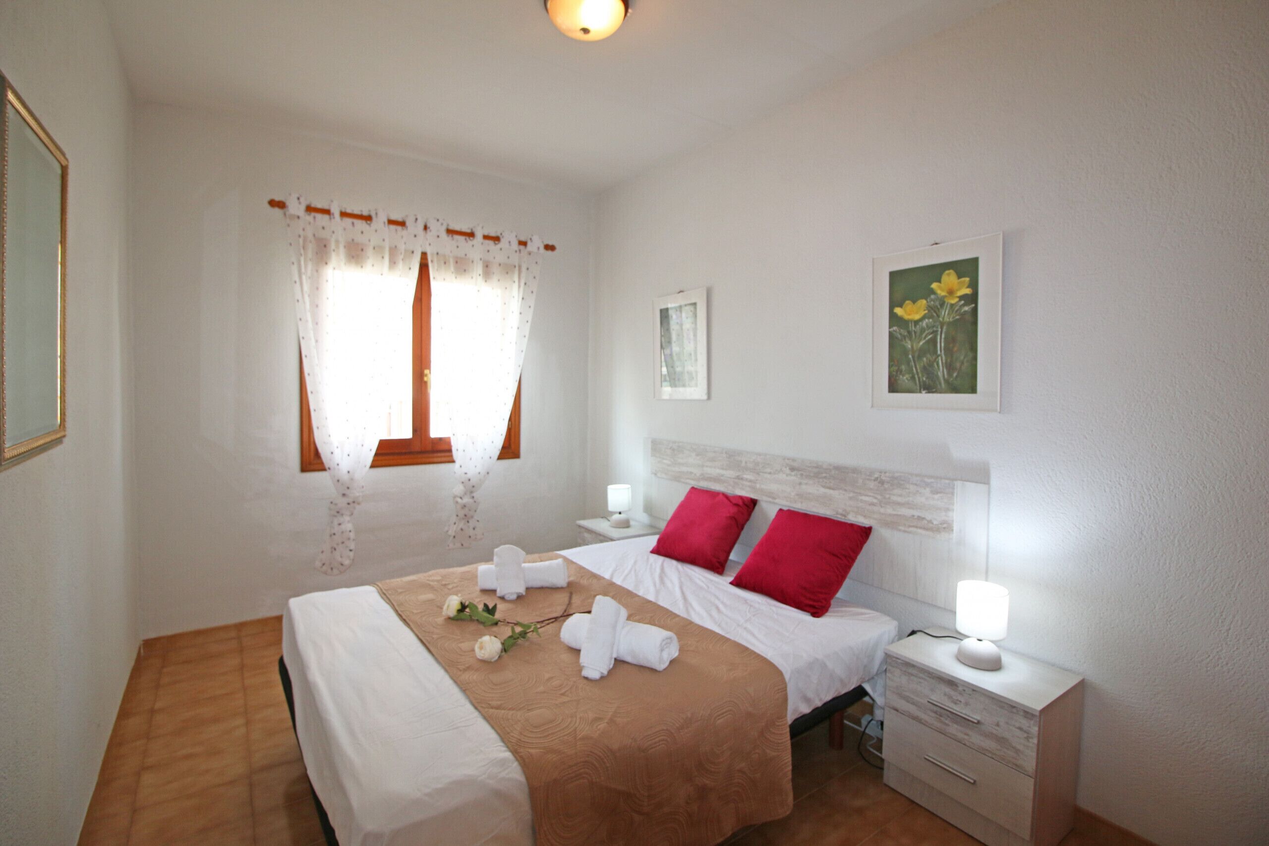 A neatly arranged bedroom with a bed, two bedside tables, a nightstand, and a window with curtains.