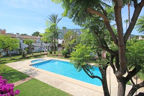 A swimming pool surrounded by lush greenery and palm trees, with a view of distant hills. - TROPICANA (Denia)