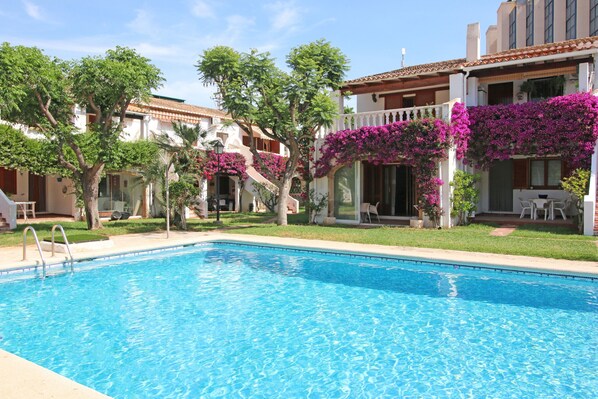 A swimming pool with a clear blue water surface, surrounded by a well-maintained lawn and trees. - TROPICANA (Denia)