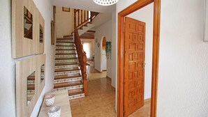 Un couloir avec une porte en bois, un escalier recouvert de carreaux décoratifs et un luminaire.