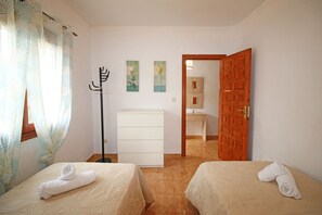 A hotel room with two beds, a wardrobe, a coat rack, and a door leading to a bathroom. - TROPICANA (Denia)