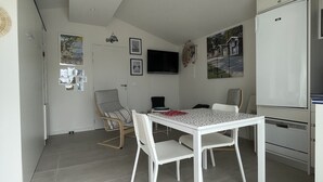 A modern kitchen with white appliances, a dining area with a table and chairs, and a TV mounted on the wall. - Cozy chef's'apartment in Hyper center... (Andernos-les-Bains)