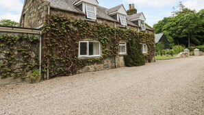 A stone building with ivy-covered walls, multiple windows, and a gravel driveway. - Storkery Cottage (Aberdeen)