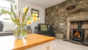 A living room with a stone wall, a fireplace, a sofa, and a vase with flowers on a table. - Storkery Cottage (Aberdeen)