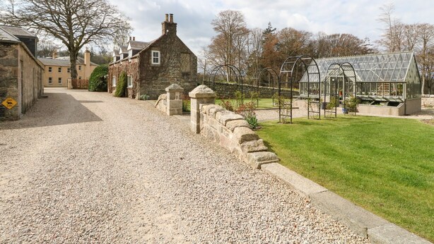 A gravel driveway leading to a stone building with a glass greenhouse structure. - Storkery Cottage (Aberdeen)