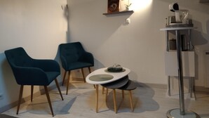 Quarto pequeno e moderno com duas cadeiras azuis, uma mesa redonda branca e um abajur.
