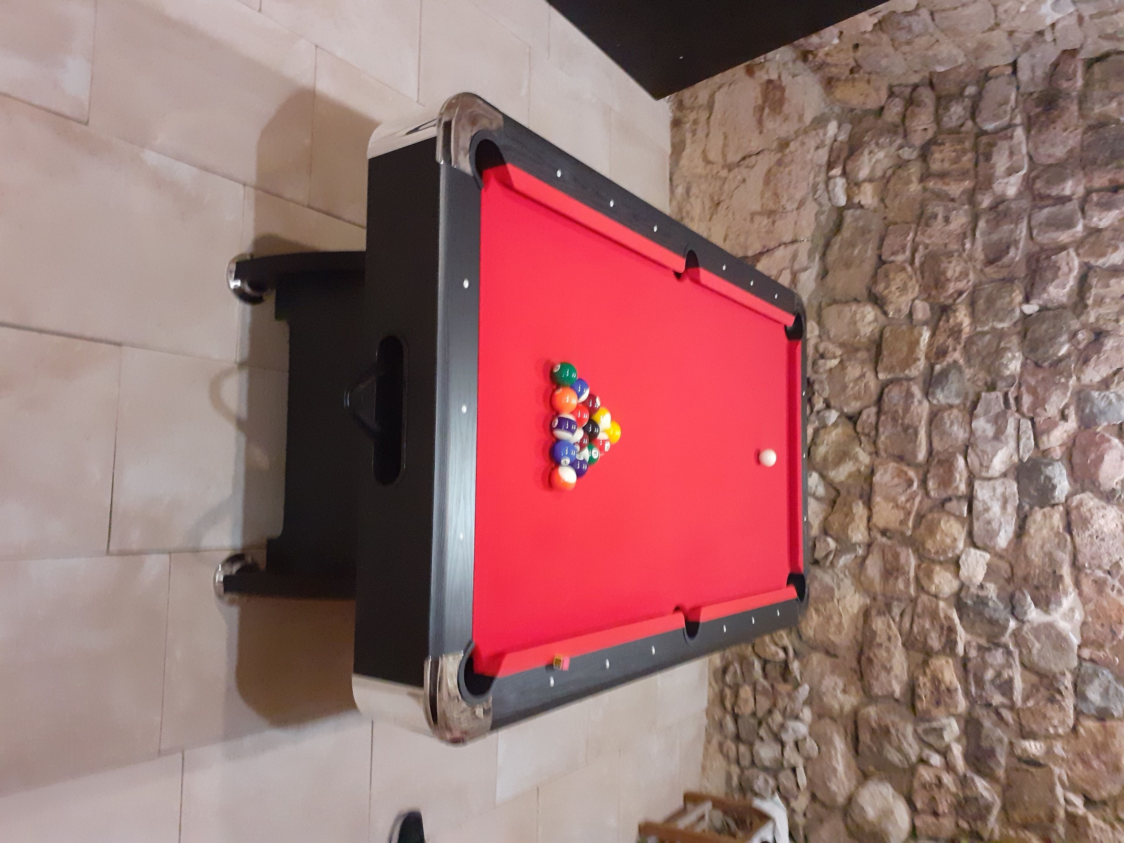 A pool table with balls, a stone wall, and a tiled floor.