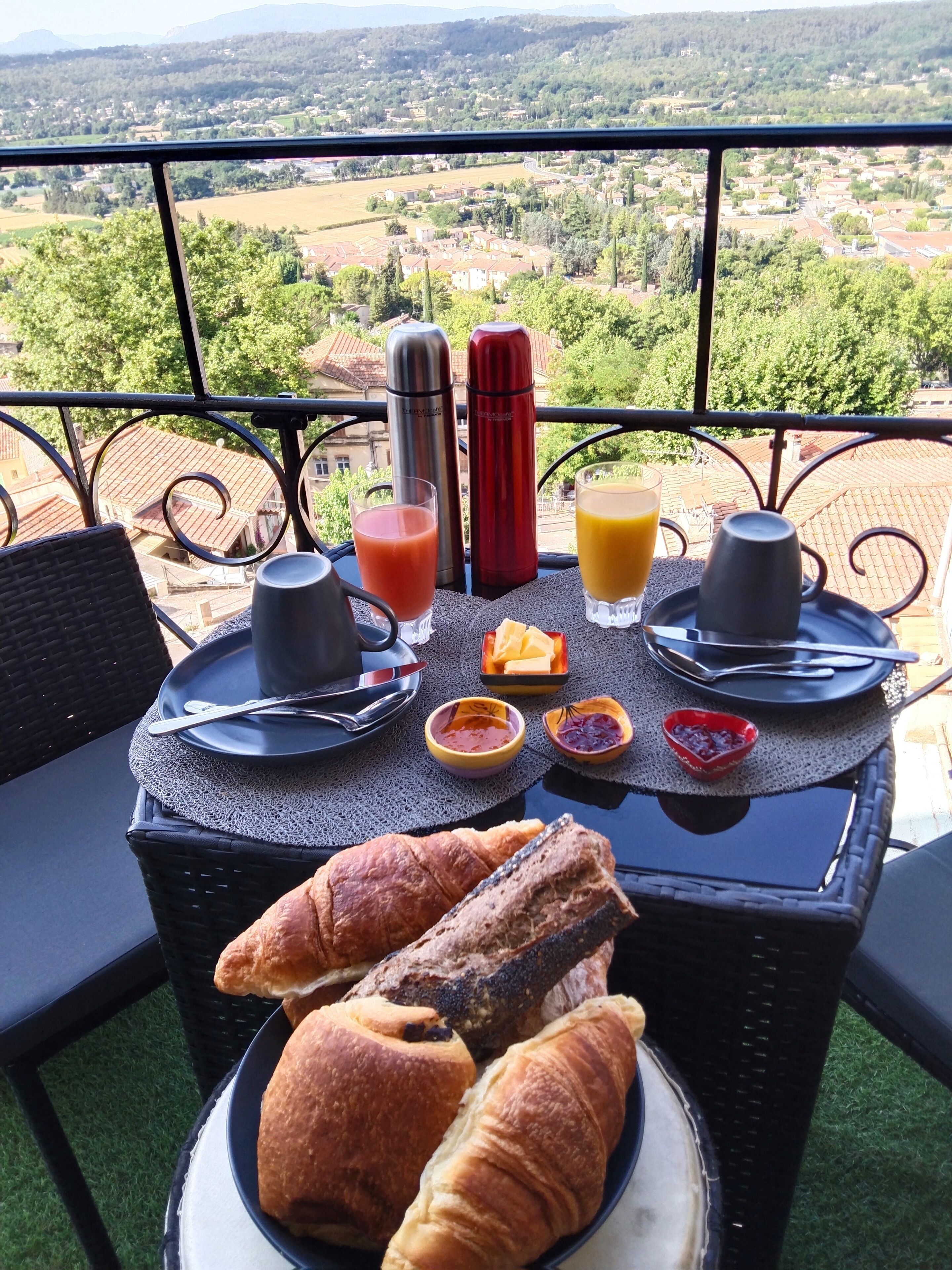 A table set with breakfast items, including croissants, juice, and butter, overlooking a scenic landscape.