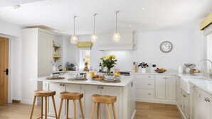 Una cocina moderna con armarios blancos, una isla central con taburetes, iluminación colgante y un reloj en la pared.
