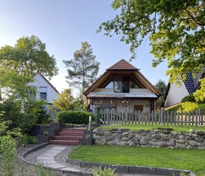A two-story house with a stone wall, a wooden fence, and a red brick staircase leading to the front door.