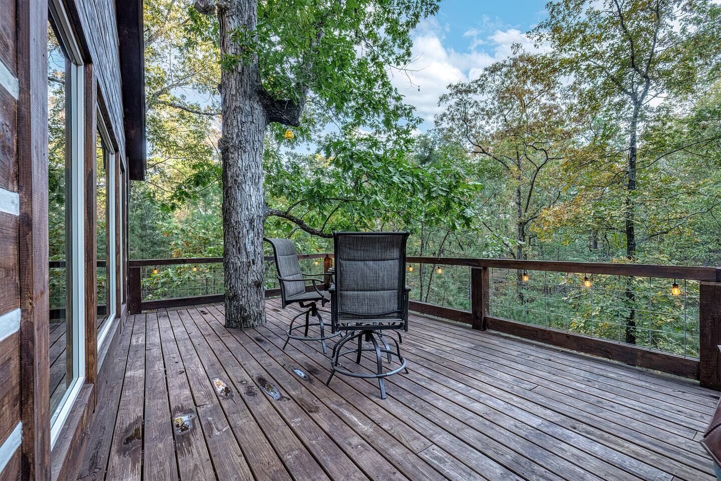 A wooden deck with two chairs and a table, surrounded by trees and a clear sky.