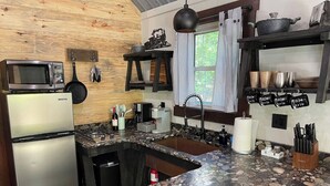 A kitchen with a granite countertop, stainless steel appliances, and a hanging pot rack. - Runaway Train Cabin at Fox Pass Cabins (Garland County)