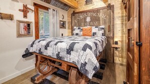 A bedroom with a bed, wooden walls, a wooden ceiling, a cross on the wall, and a sign reading "Union Pacific Railway". - Runaway Train Cabin at Fox Pass Cabins (Garland County)