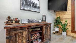 A rustic wooden cabinet with vintage train models and a black and white photo. A flat-screen TV is mounted on the wall above. - Runaway Train Cabin at Fox Pass Cabins (Garland County)
