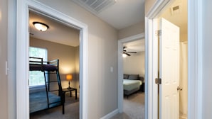 Un pasillo que conduce a un dormitorio con literas, ventilador de techo y ventana con persianas.
